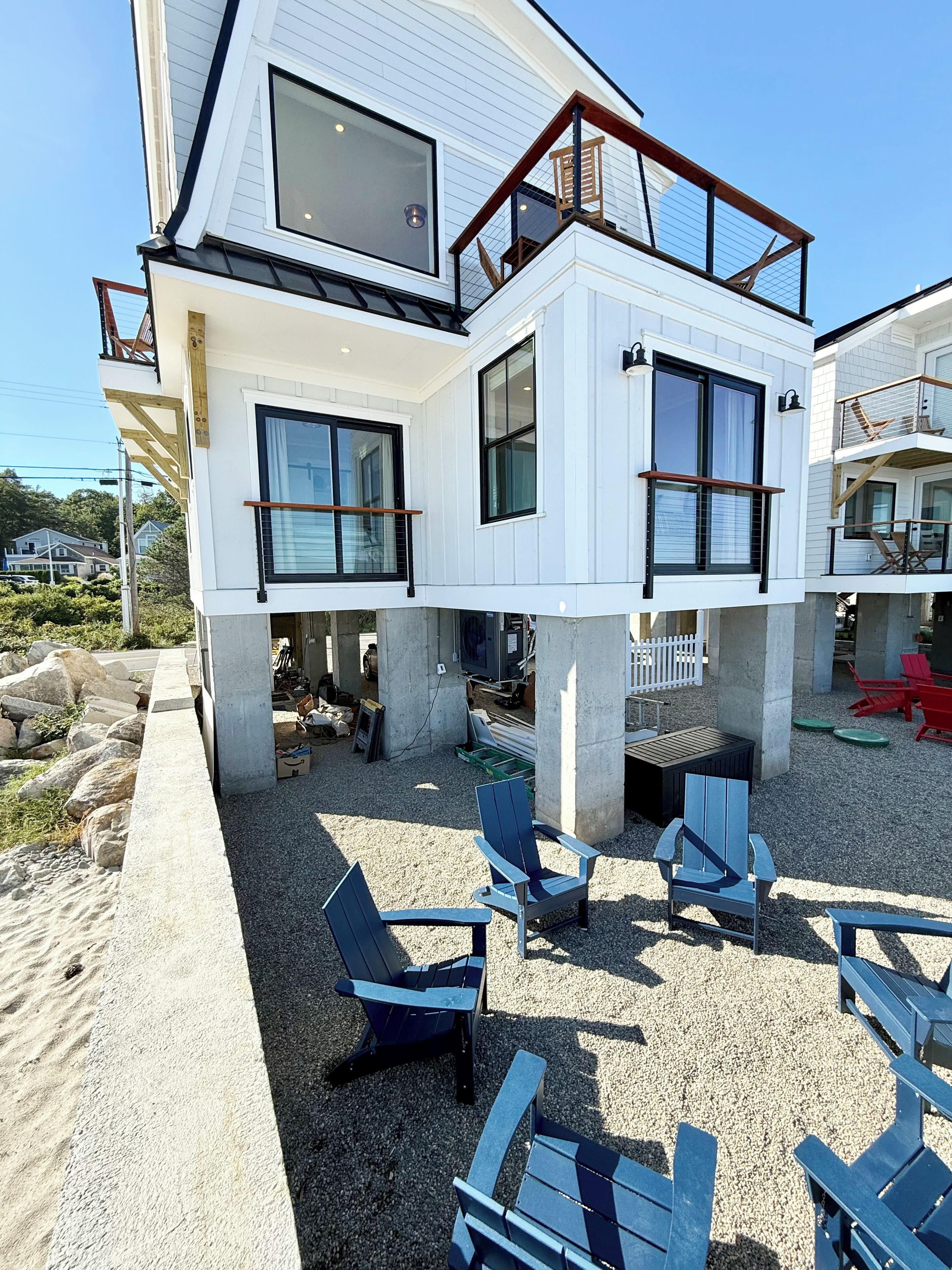 A modern two-story house with a balcony, outdoor seating area, and a view of the surrounding landscape.