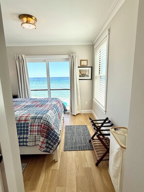 A bedroom with a bed, a window with curtains, a wooden floor, and a ceiling light fixture.