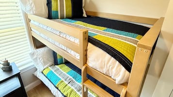 A bunk bed with a quilted bedspread, a wooden headboard, and a window with blinds.