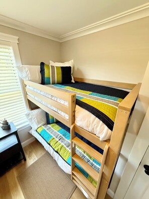 A bunk bed with a quilted bedspread, a wooden headboard, and a window with blinds.