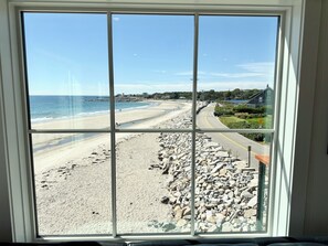 A beach view through a window with a clear sky, a sandy beach, and a road with a curve.