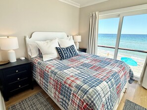 A bedroom with a bed, nightstands, a view of the beach, and a balcony.
