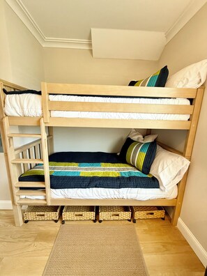 Una cama litera con colcha a rayas y almohadas, una escalera de madera y un tapete tejido en el suelo.