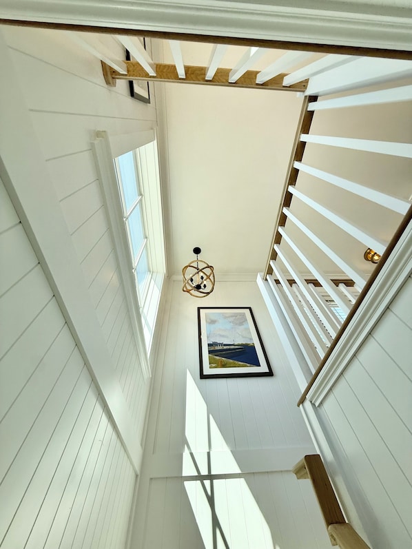 A narrow hallway with white walls and wooden beams, a framed picture on the wall, and a hanging light fixture.
