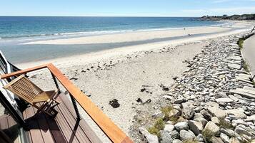A beach with a wooden deck and a chair, overlooking a sandy beach and rocky shoreline.