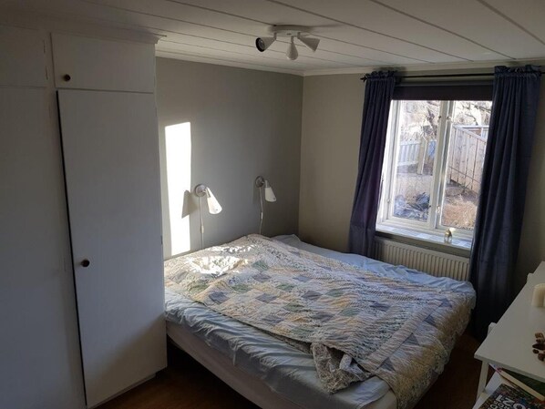 A bedroom with a bed, a window with curtains, a radiator, and a door.
