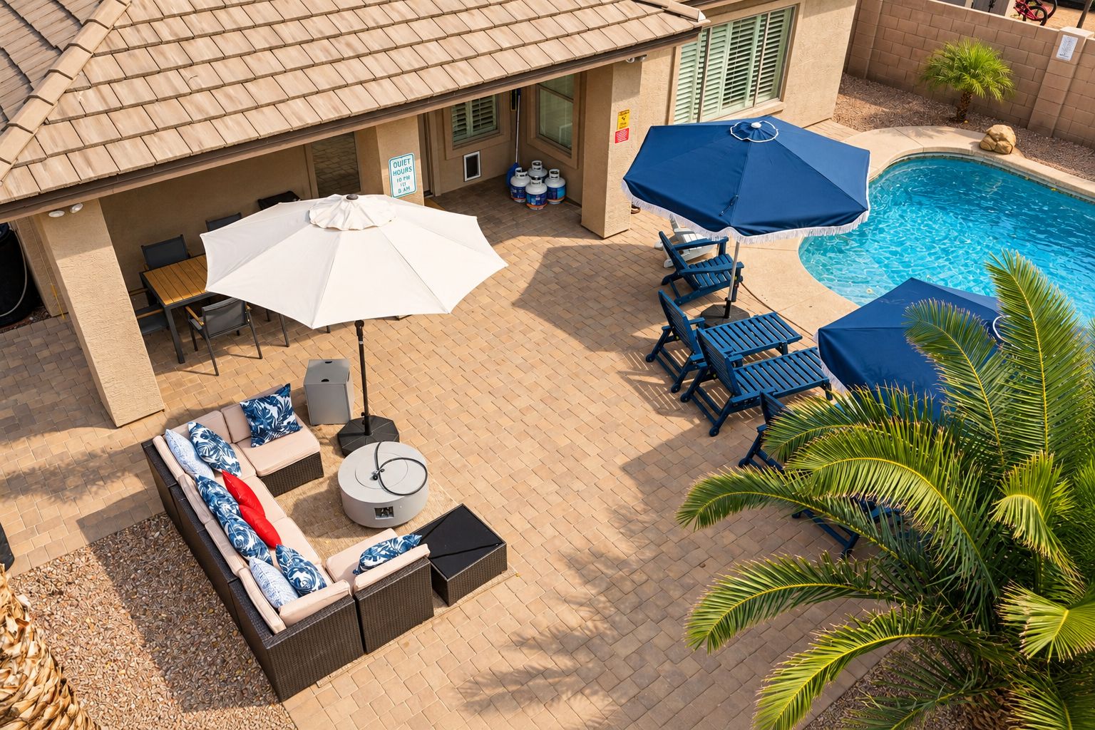 An outdoor patio with a pool, lounge chairs, and a table with an umbrella.