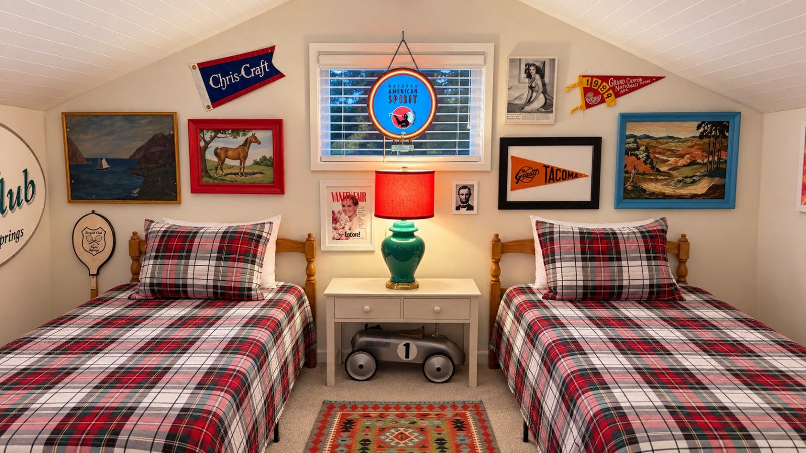A bedroom with two beds, a window with blinds, a lamp, and various framed pictures on the wall.