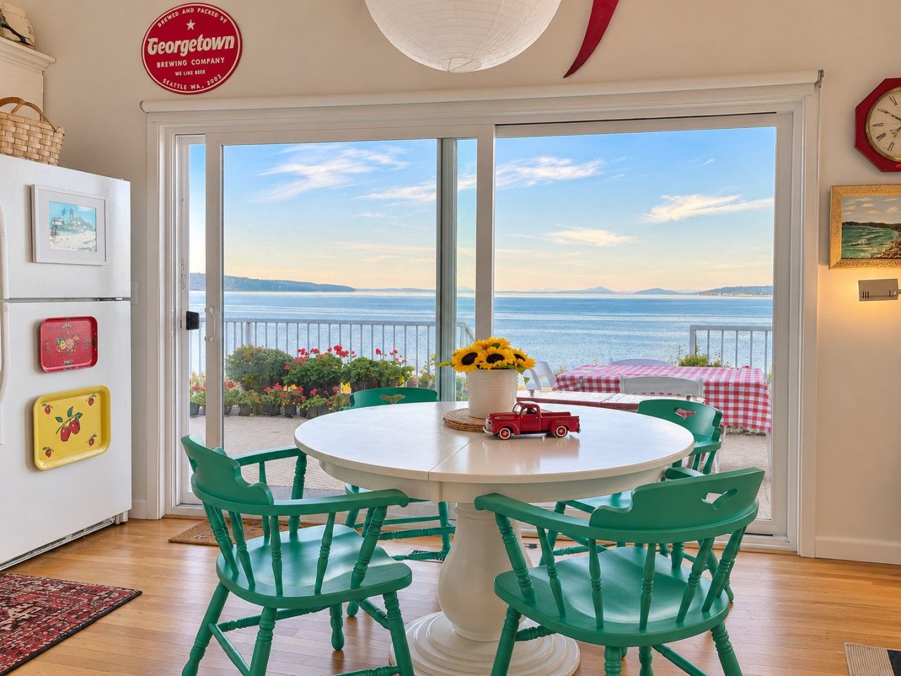 A room with a large window overlooking a scenic view, a round table with chairs, and a small red toy car on the table.