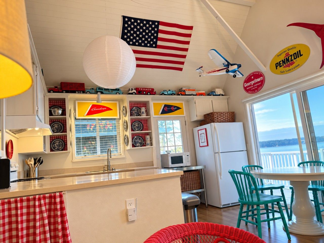 A kitchen with a central island, a dining area with green chairs, a refrigerator, and a view of the water.