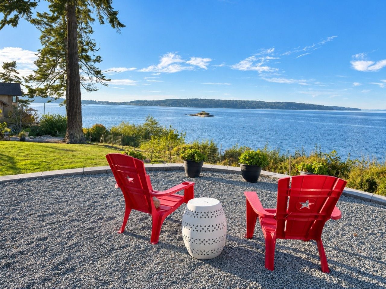 An outdoor seating area with two red chairs and a white table, overlooking a body of water.