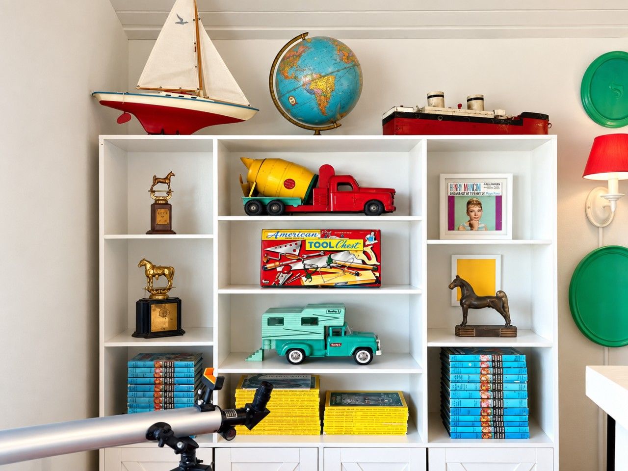 A bookshelf with various items including a toy sailboat, a globe, a toy cement mixer, and books.