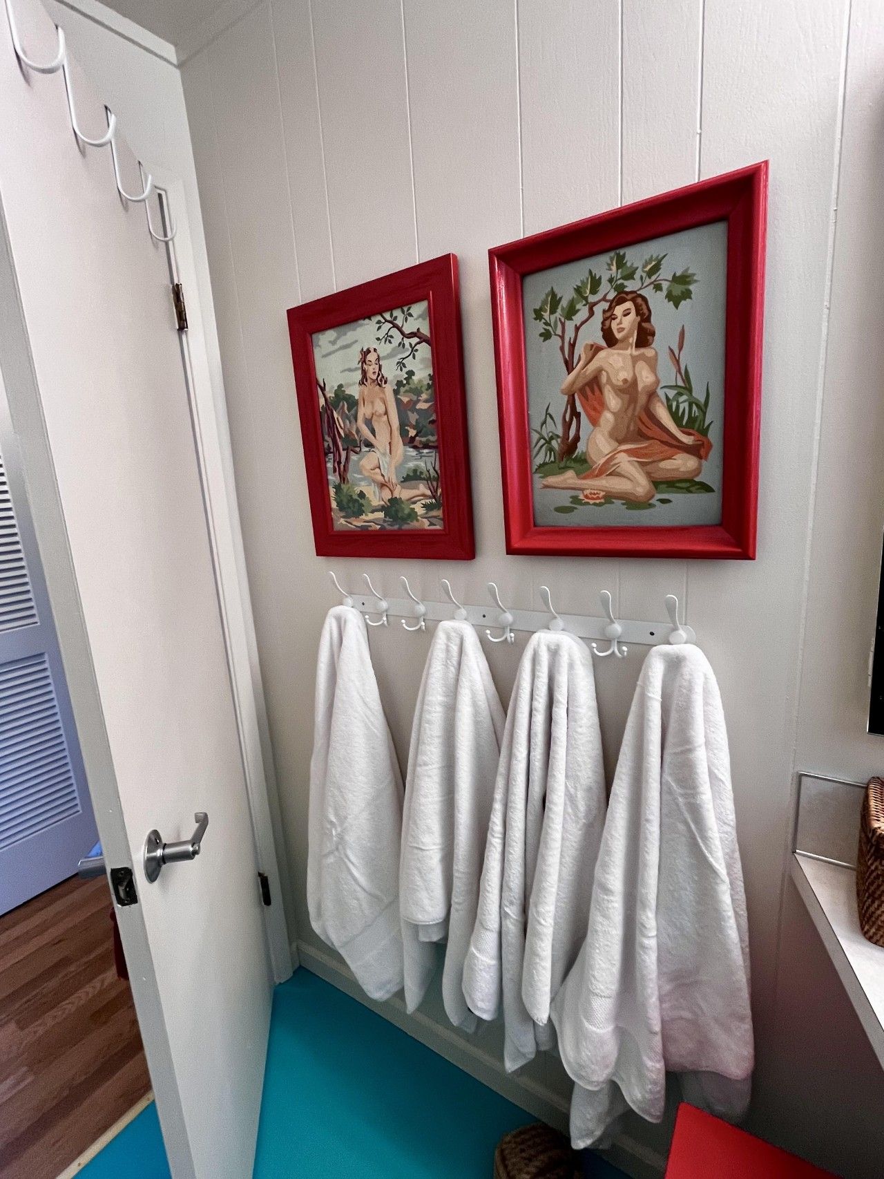 A bathroom with two framed paintings, a towel rack with white towels, and a wooden floor.
