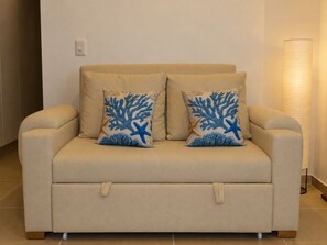 A beige sofa with two decorative pillows featuring blue coral and starfish designs. - Moesko Apartment (Gaira)