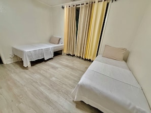 Une chambre avec deux lits, une table et une fenêtre avec des rideaux.