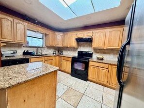 A kitchen with wooden cabinets, a black stove, a dishwasher, and a refrigerator.