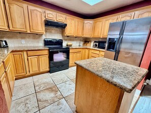A kitchen with wooden cabinets, a black stove, a stainless steel refrigerator, and a granite countertop.