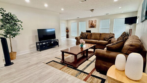 A living room with a flat-screen TV, a brown sofa, a coffee table, and a potted plant.