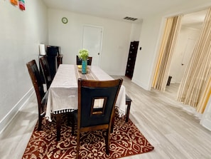 A dining area with a table, chairs, a clock, and a door.