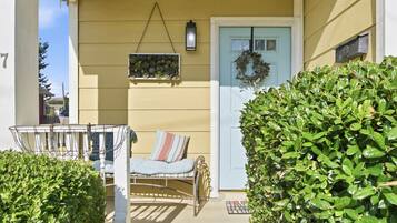 A porch with a cushioned bench, a hanging planter, and a door with a wreath.
