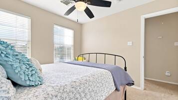 A bedroom with a bed, a ceiling fan, and two windows with blinds.
