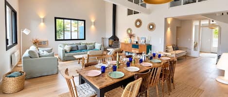 A spacious living room with a dining area, large windows, and a high ceiling.