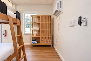 Een kamer met een stapelbed, een houten garderobe, een nachtkastje, een lamp en een wandgemonteerde airconditioner.