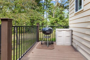 Ein Grill auf einer Holzterrasse mit einem Metallzaun und einem Stauraum.