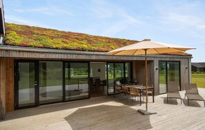 Un espace de restauration extérieur moderne, doté d’une structure vitrée, d’une terrasse en bois et d’un toit végétalisé.