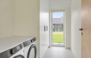 A laundry room with a front-loading washing machine, a door leading to a balcony, and a view of a building with a tiled roof. - Stunning home in Haderslev with WiFi (Haderslev)