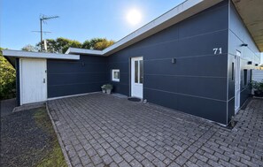 En modern byggnad med en mörk fasad, en vit dörr och husnummer 71.