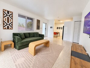 A modern living room with a green sofa, a wooden bench, and a dining area with red chairs. - Stylish 2BR Near Wynwood | Pool + Free Parking (Miami)