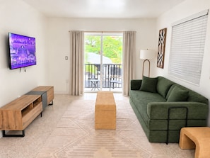 A modern living room with a flat-screen TV, a green sofa, a wooden coffee table, and a patterned rug. - Stylish 2BR Near Wynwood | Pool + Free Parking (Miami)