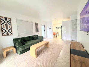 A modern living room with a green sofa, a wooden bench, and a patterned rug. - Stylish 2BR Near Wynwood | Pool + Free Parking (Miami)