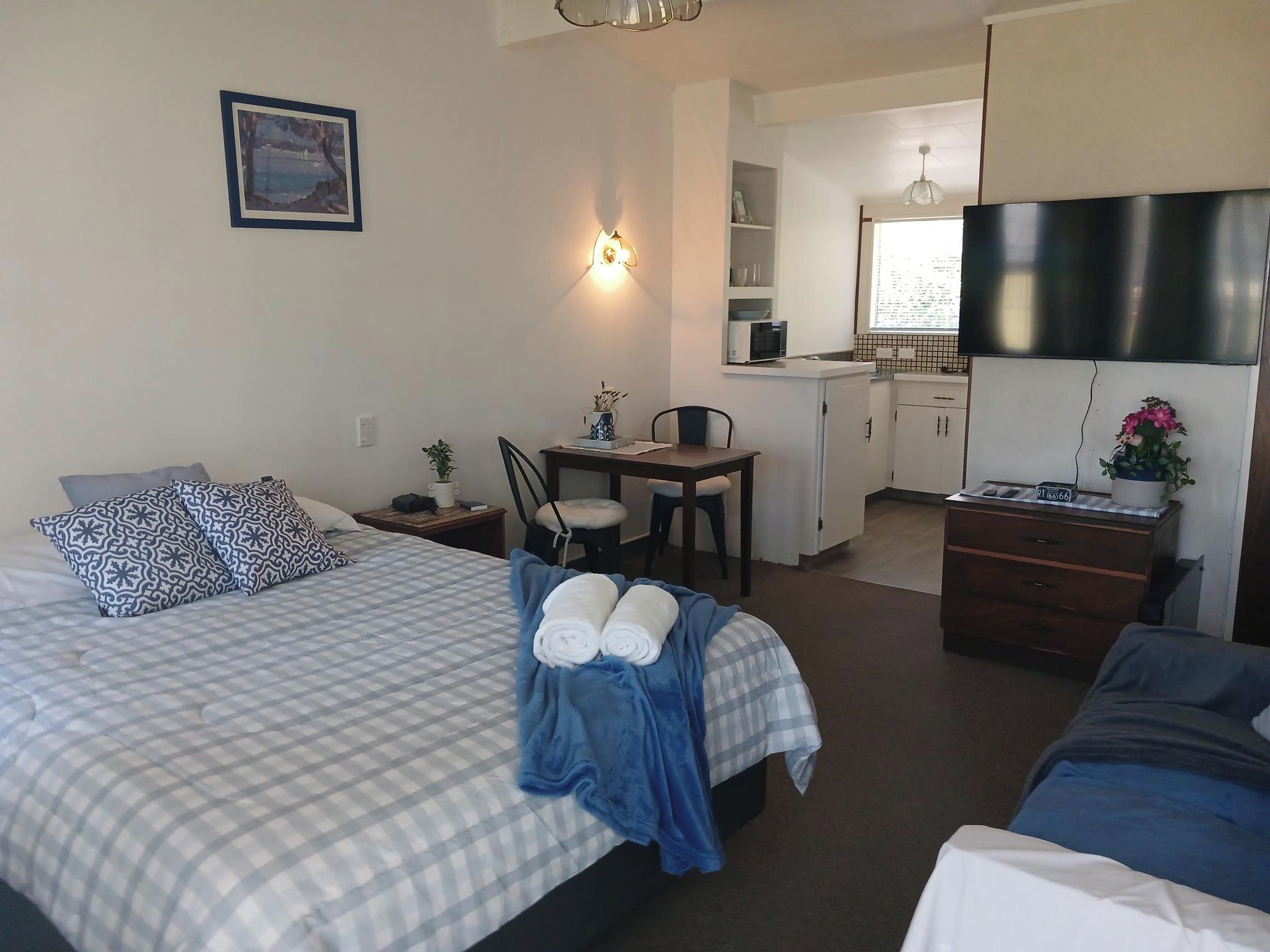 A hotel room with a bed, a desk, a chair, a dresser, a microwave, and a television.