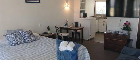 A hotel room with a bed, a desk, a chair, a dresser, a microwave, and a television.