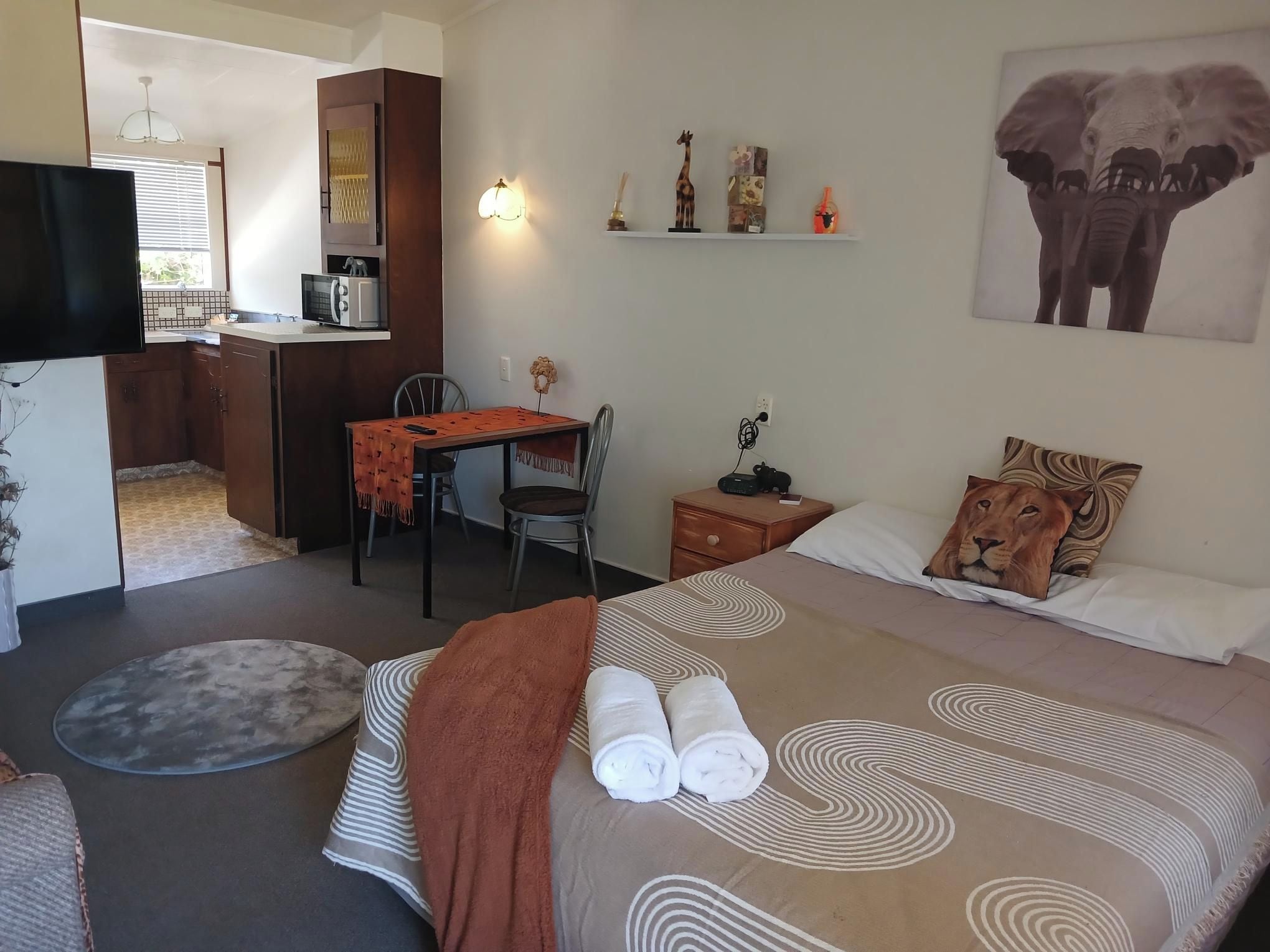 Habitación de hotel con cama, escritorio, silla, mesita, mesita de noche, televisor y un muro con adornos.