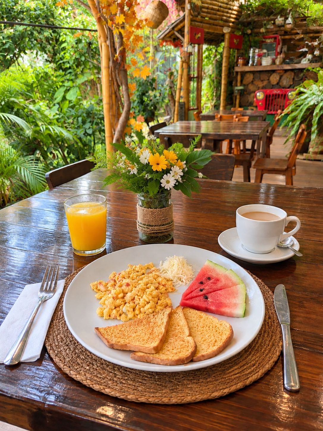Een ontbijtsetting met een bord eten, een glas jus d'orange, een kop koffie en een bloevas.