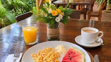 Een ontbijtsetting met een bord eten, een glas jus d'orange, een kop koffie en een bloevas.