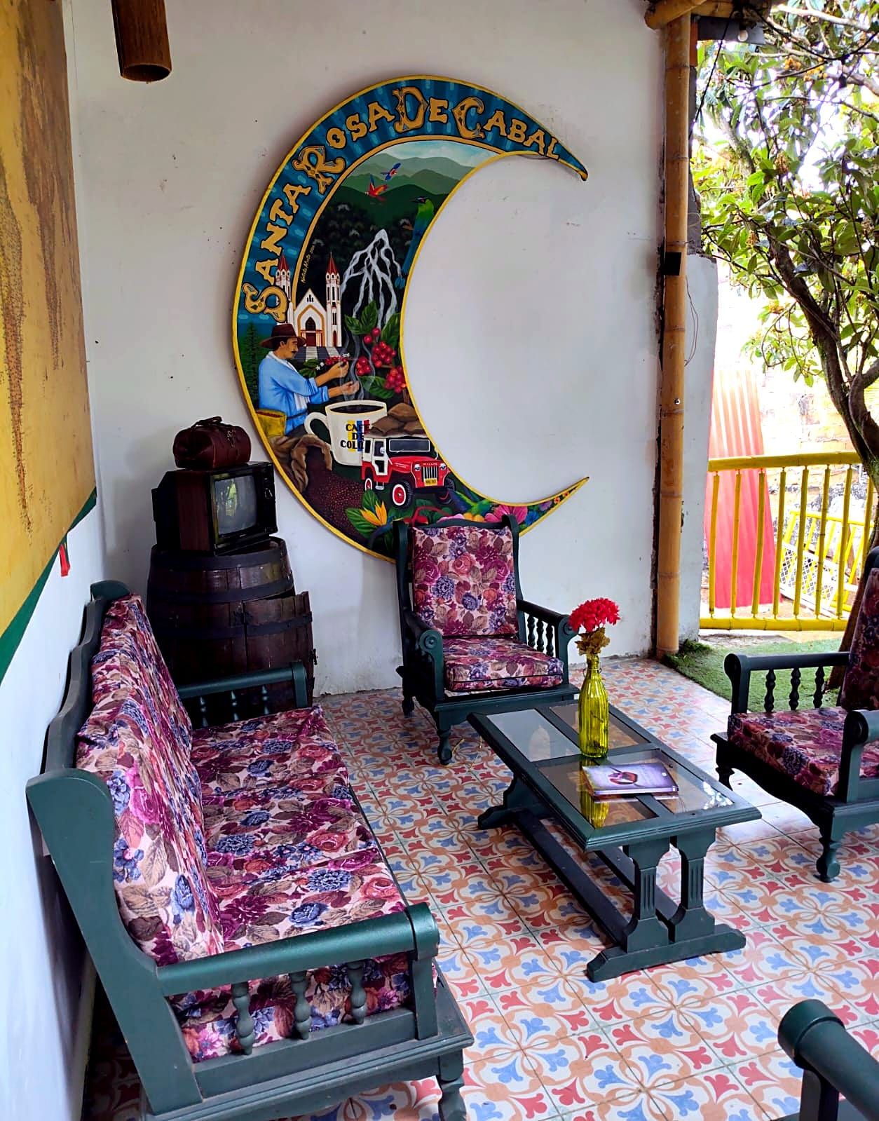 Una habitación con un mural, dos sillones tapizados, una mesita con un florero y un televisor sobre un mueble bajo.