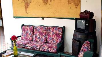 A room with a large world map on the wall, a floral sofa, a wooden coffee table, and a vintage television.