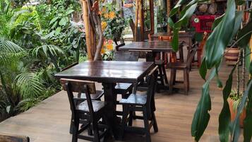 An outdoor dining area with wooden tables and chairs, surrounded by lush greenery and autumn foliage.
