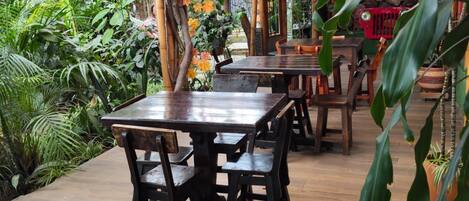 An outdoor dining area with wooden tables and chairs, surrounded by lush greenery and autumn foliage.