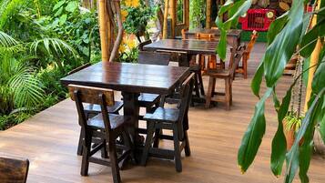 Een terras buiten met houten tafels en stoelen, omringd door weelderige begroeiing en bamboestructuren.
