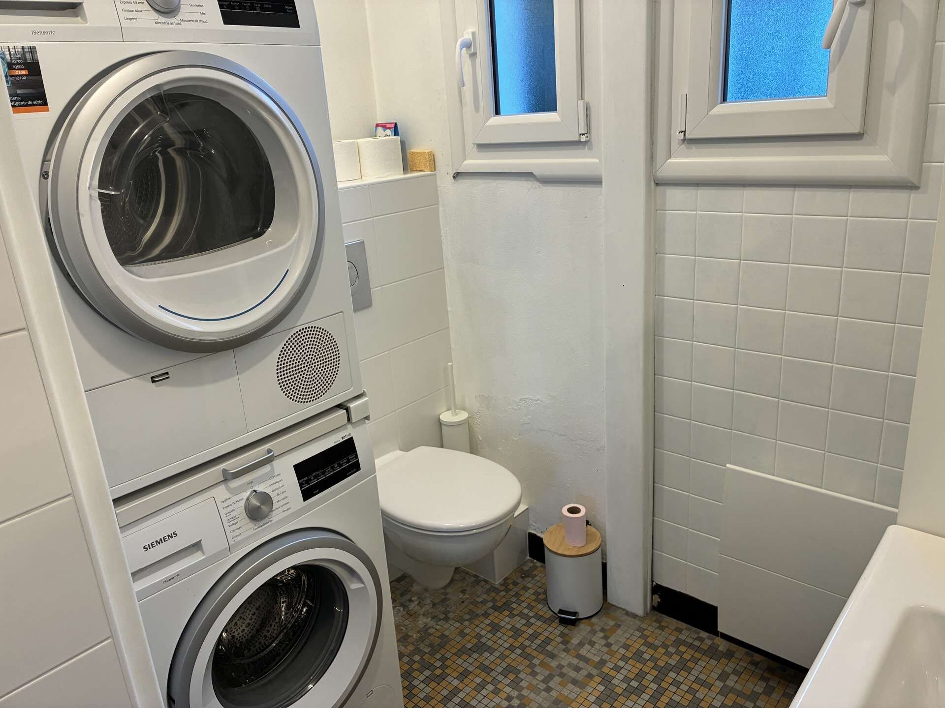 A compact bathroom with a washing machine, a toilet, and a window.