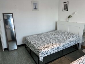 A single bed with a leaf-patterned bedspread in a room with white walls, a radiator, and a framed picture on the wall. - Les Carolines de Sion (SAINT HILAIRE DE RIEZ)