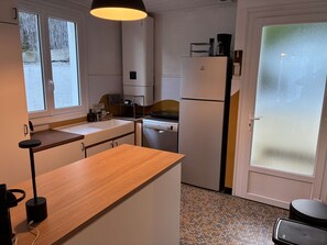Kompakti keittiö, jossa on puinen työtaso, sisäänrakennettu uuni, jääkaappi ja ikkuna, jossa on himmeä lasi.