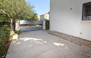 Un patio empedrado con una reja de metal, un árbol y un edificio con ventana.