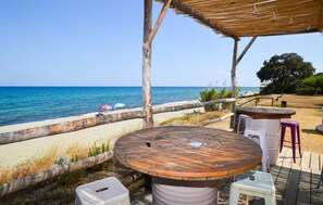 Zona salotto all'aperto sulla spiaggia, con tavolo e sedie in legno, vista mare.