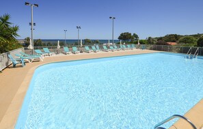 Ein Schwimmbecken mit Liegestühlen und Sonnenschirmen, umzäunt mit Blick aufs Meer.